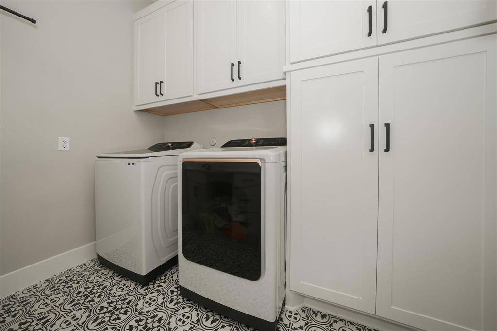 This laundry room features modern appliances with a sleek design, ample white cabinetry for storage, and a stylish black-and-white patterned tile floor, creating a clean and functional space.
