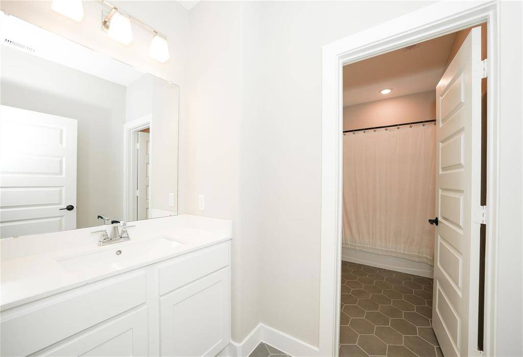 This bathroom features a modern design with a spacious vanity and large mirror. The area includes a shower with a curtain and hexagonal floor tiles, offering a clean and stylish look.