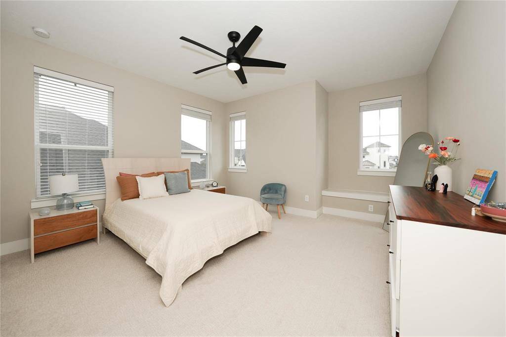 This bright, spacious bedroom features neutral walls, large windows for natural light, and a ceiling fan. It includes a cozy bed with modern side tables, a stylish dresser, and a comfortable chair, creating a welcoming and functional retreat.