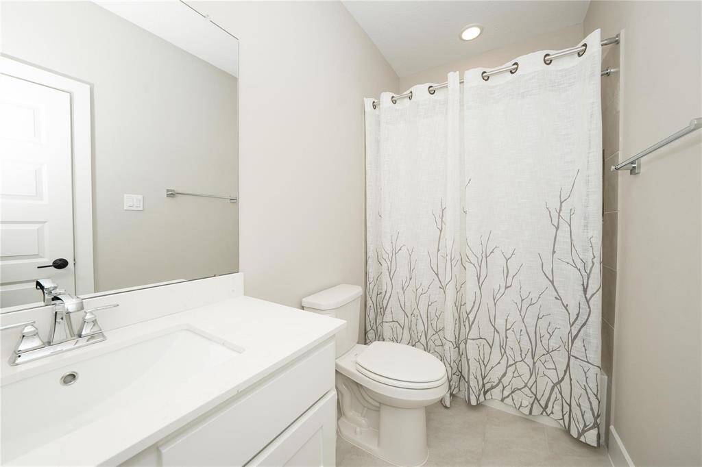 This bathroom features a clean, modern design with a white vanity, a large mirror, and a shower with a decorative curtain. The neutral color palette creates a bright and inviting space.