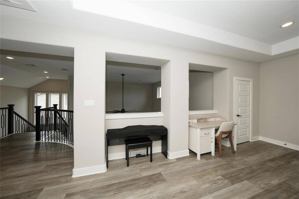 This photo showcases a spacious upstairs area with modern laminate flooring, an open railing staircase, and two niche spaces—one with a small desk setup. The neutral color palette and recessed lighting add a contemporary feel.