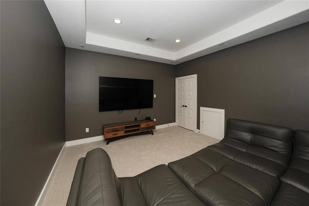 This cozy home theater room features dark walls, recessed lighting, and a large wall-mounted TV. It is furnished with comfortable leather seating and has a carpeted floor, creating an inviting space for entertainment.