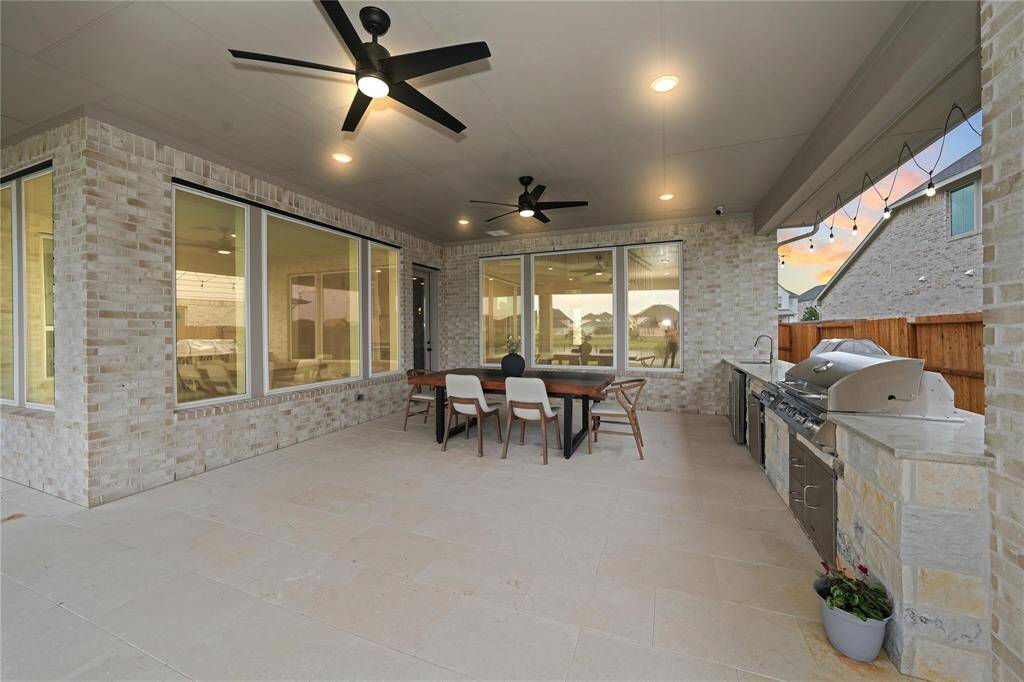 This photo showcases a spacious, covered patio with a modern outdoor kitchen, featuring a grill and ample counter space. It has large windows, ceiling fans, and stylish lighting, creating an inviting space for outdoor dining and entertaining.