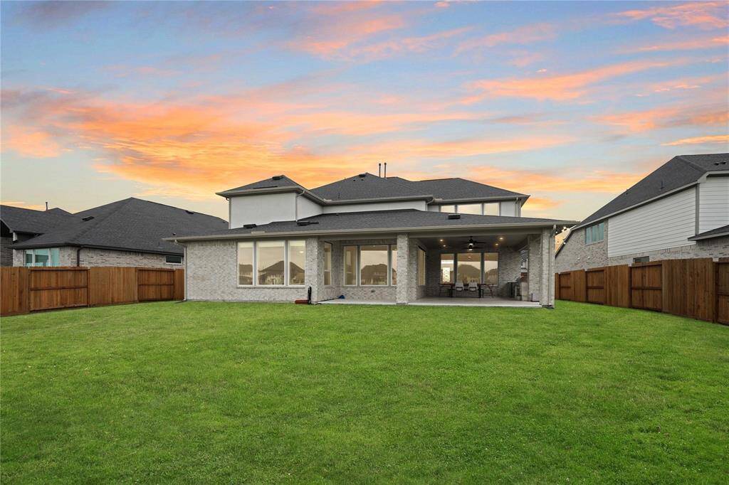Spacious backyard with a covered patio, perfect for outdoor gatherings. The house features a modern exterior with large windows and well-maintained lawn, set against a beautiful sunset.