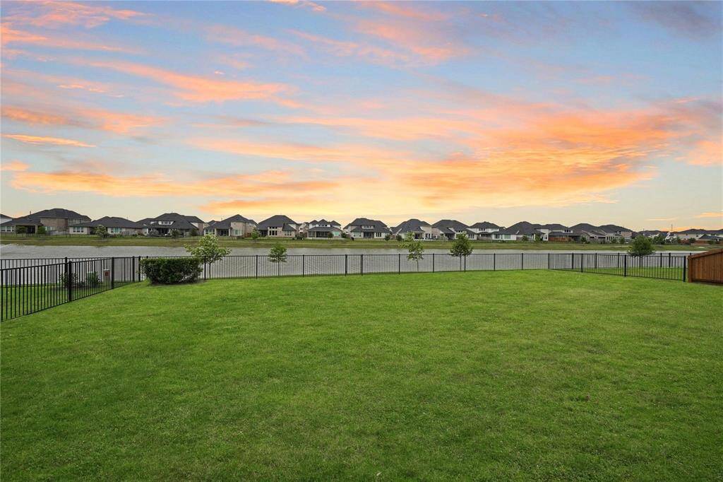 Spacious backyard with well-maintained lawn, overlooking a serene pond and neighborhood homes. Perfect for outdoor activities and enjoying beautiful sunsets.