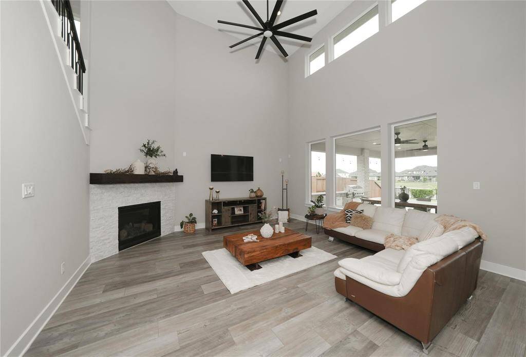 This spacious living room features high ceilings, modern gray flooring, and large windows for natural light. It includes a sleek fireplace, a wall-mounted TV, and an inviting seating area, creating a cozy yet stylish ambiance.
