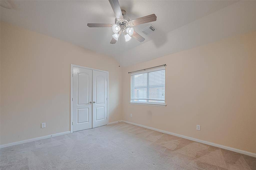 Secondary bedroom features plush carpet, custom paint, dark stained ceiling fan with lighting and a large window with privacy blinds.