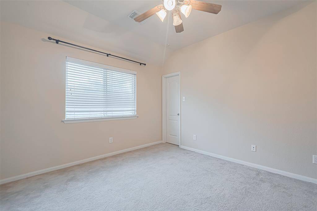 Secondary bedroom features plush carpet, custom paint, dark stained ceiling fan with lighting and a large window with privacy blinds.