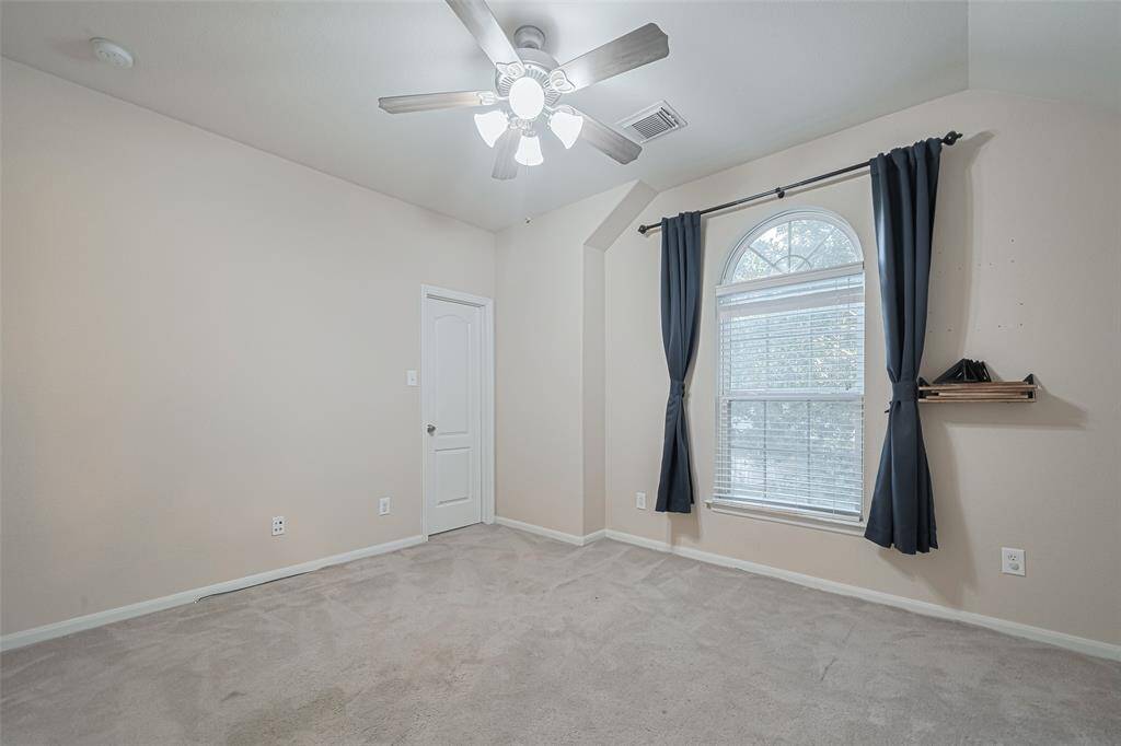 Secondary bedroom features plush carpet, custom paint, dark stained ceiling fan with lighting and a large window with privacy blinds.