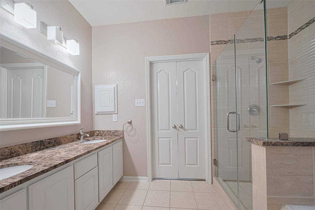 This primary bathroom is definitely move-in ready! Featuring a framed walk-in shower with tile surround, separate garden tub for soaking after a long day with custom tile detailing, light  stained cabinets, spacious walk-in closet with shelving, high ceilings, custom paint, sleek and modern finishes