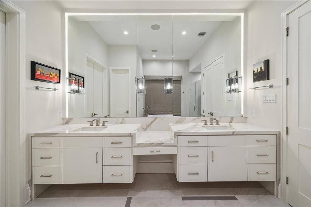 The primary bathroom features a sleek dual-sink vanity with quartzite countertops, polished nickel fixtures, and elegant custom lighting. This serene space combines luxury with functionality.