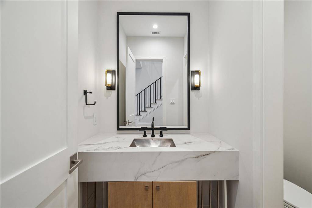 The first-floor powder room boasts a custom vanity with quartzite countertops, designer lighting, and a polished nickel mirror. Its elegant details elevate this functional space.