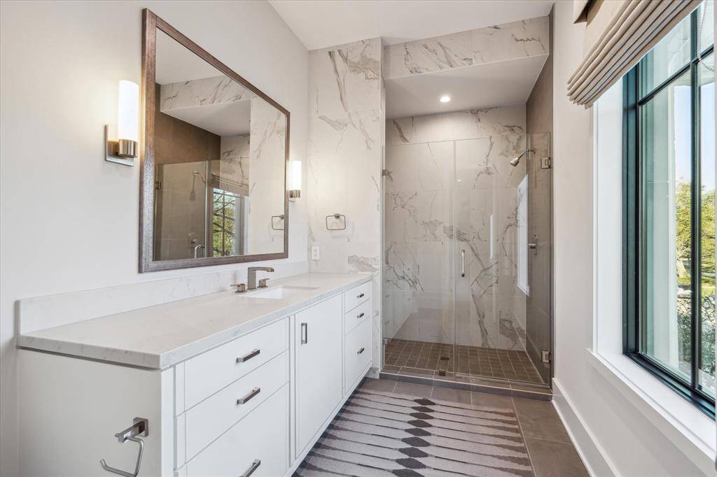 Guest bathroom #1 features designer grey tile flooring, quartzite countertops, and a walk-in shower with porcelain tile detailing. Sleek finishes and thoughtful design create a timeless space.