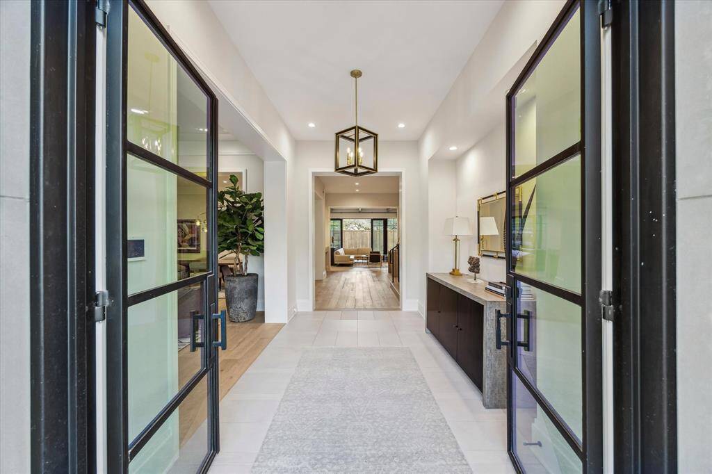The grand foyer greets you with designer tile flooring, a striking brass and blackened steel chandelier, and elegant 12-inch door casings. This inviting entry seamlessly connects to the formal living and dining rooms, creating a graceful flow for entertaining. The thoughtful layout offers both function and timeless design.