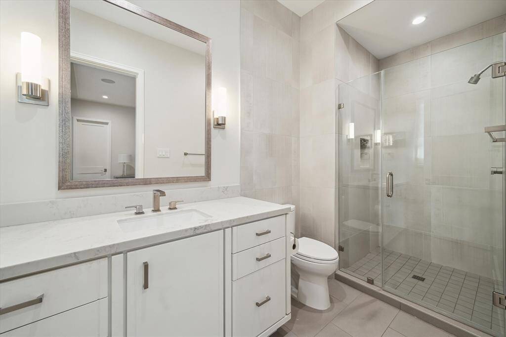 Guest bathroom #3 features designer grey tile flooring, brushed nickel fixtures, and a seamless glass walk-in shower. Sleek finishes enhance the space’s polished design.