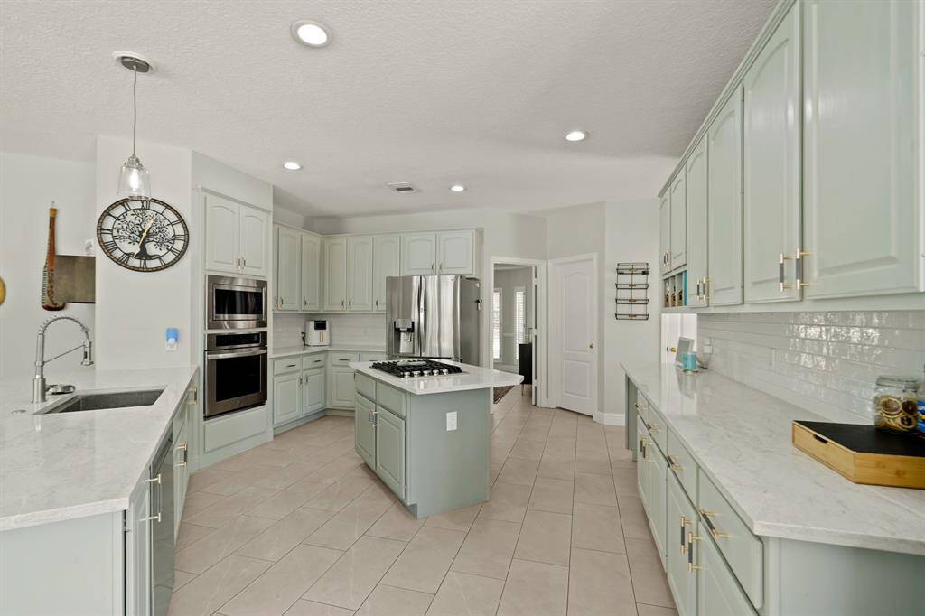 This modern kitchen features sleek, light-colored cabinetry, stainless steel appliances, and ample counter space with a central island. The room is well-lit with recessed lighting and a pendant over the sink, creating a bright and inviting atmosphere.