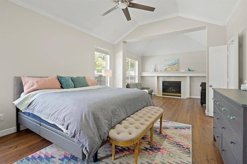 This spacious bedroom features a cozy fireplace, vaulted ceilings, and large windows for natural light. The room is elegantly designed with hardwood floors, a ceiling fan, and a comfortable sitting area, offering both style and functionality.