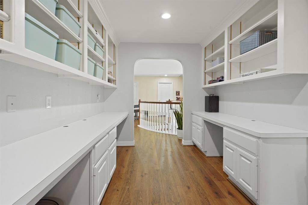 Bright and spacious 2nd-floor hallway office with built-in shelves and cabinets, featuring hardwood floors and recessed lighting. Perfect for a home office or storage space.