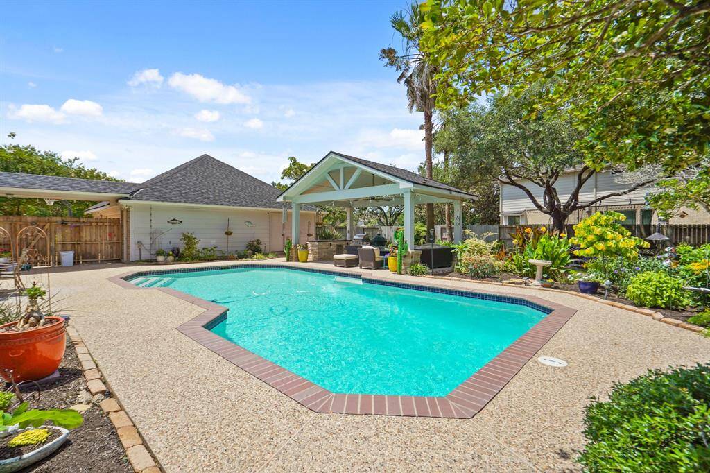 This photo showcases a spacious backyard with a sparkling pool surrounded by lush greenery. The patio area features a covered seating space, perfect for relaxation and entertaining.
