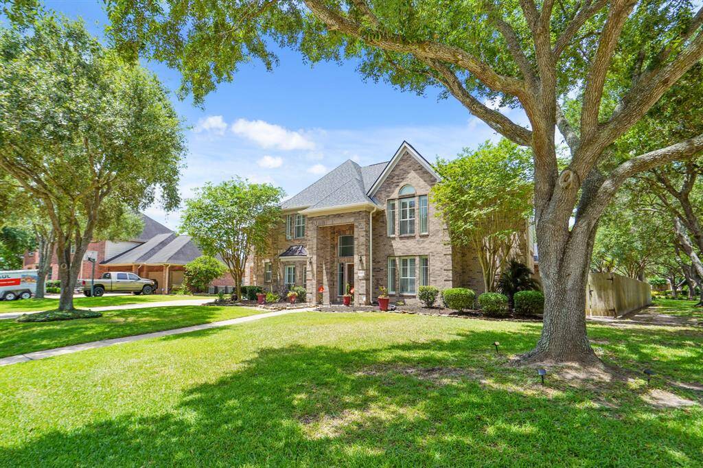 This corner lot photo showcases a charming two-story brick home with a well-maintained front yard. The property features mature trees and manicured landscaping, providing an inviting and serene atmosphere.