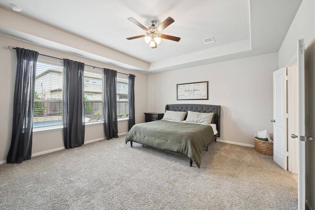 Spacious primary bedroom with windows looking out toward the pool. Beautiful ceiling and double doors leading to en-suite.