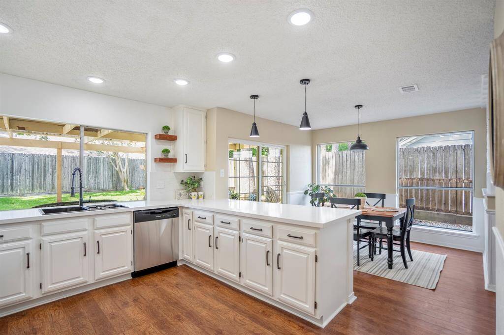 Step into the sleek updated kitchen, quartz counters and modern pendant lights create a sleek atmosphere. To the left, a large window over the sink frames the view of the covered patio, while the breakfast bar ahead separates the kitchen from the bright breakfast nook.