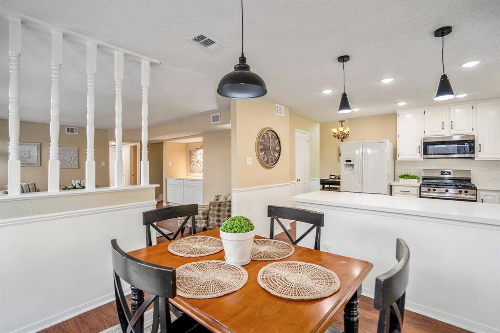 From near the back door, look across the breakfast nook into the family room, separated by a half wall topped with spindle-style balusters that provide separation while keeping the space open and connected. The kitchen is visible to the right, creating a welcoming flow throughout.