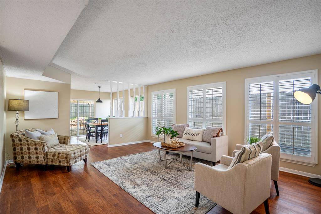 Looking back across the family room from near the dry bar, the breakfast nook is visible beyond. Luxury vinyl plank flooring flows throughout, complemented by elegant plantation shutters that frame the windows and fill the space with soft natural light.