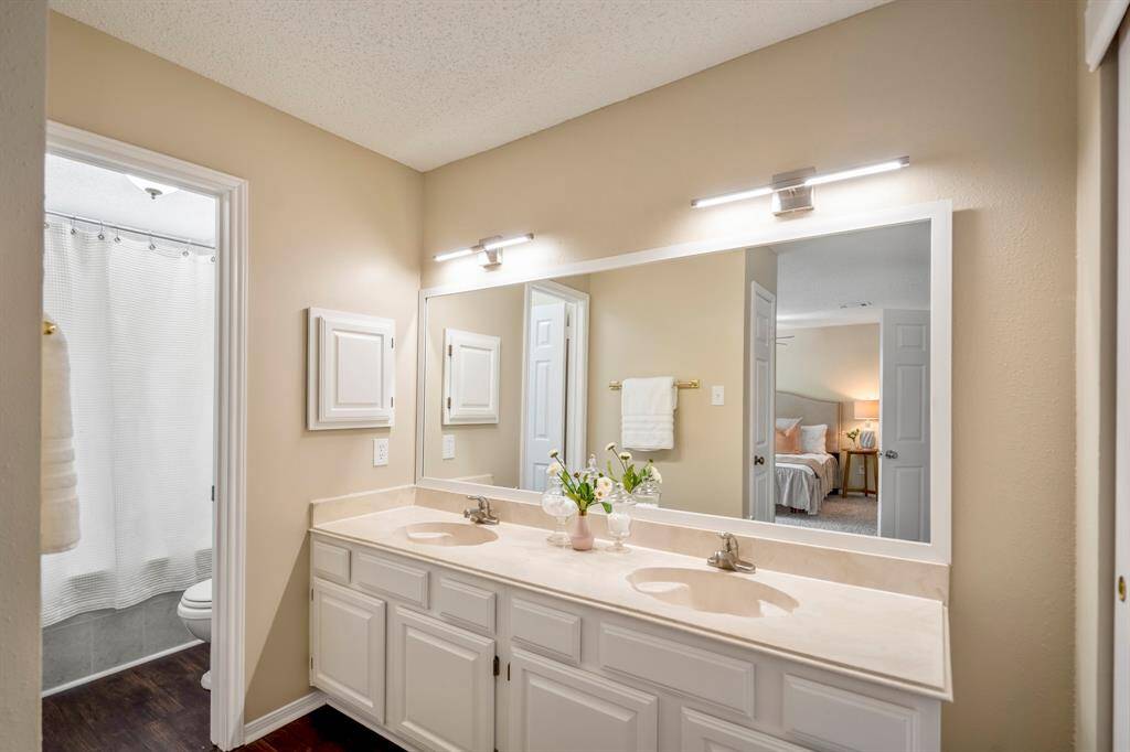 Stepping into the primary bathroom, dual sinks with modern light fixtures and a medicine cabinet offer both style and function. The shower and toilet are thoughtfully tucked behind a separate doorway for added privacy.