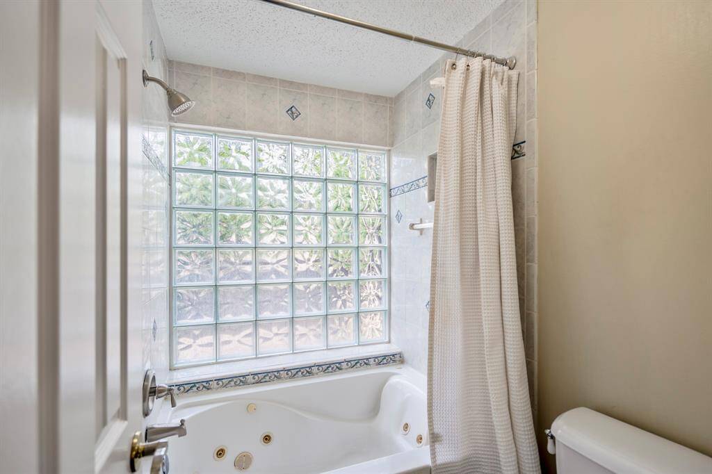 A closer look at the primary bath’s shower area reveals a spacious jetted tub and shower combo, complemented by a large block glass window that fills the space with natural light.