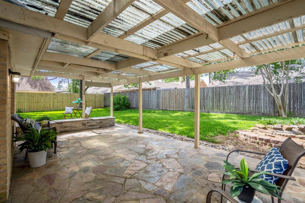 Stepping out onto the covered flagstone patio, you’ll find a granite-topped bench along the far edge, perfect for relaxed seating. The flagstone extends beyond the covered area to additional uncovered space, surrounded by a lush lawn and new fencing along the left side, creating a private and inviting outdoor retreat.