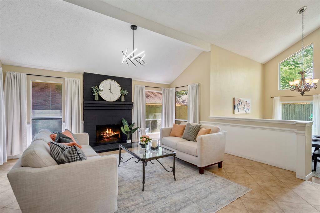 To the left of the entry, the formal living room draws you in with its striking painted brick fireplace, contemporary lighting, and walls of windows that fill the space with natural light.