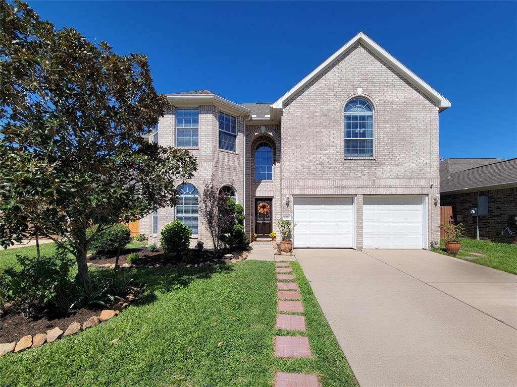 This is a two-story brick home with a double garage and well-maintained landscaping. It features a welcoming front entrance, large arched windows, and a neat pathway leading to the door.