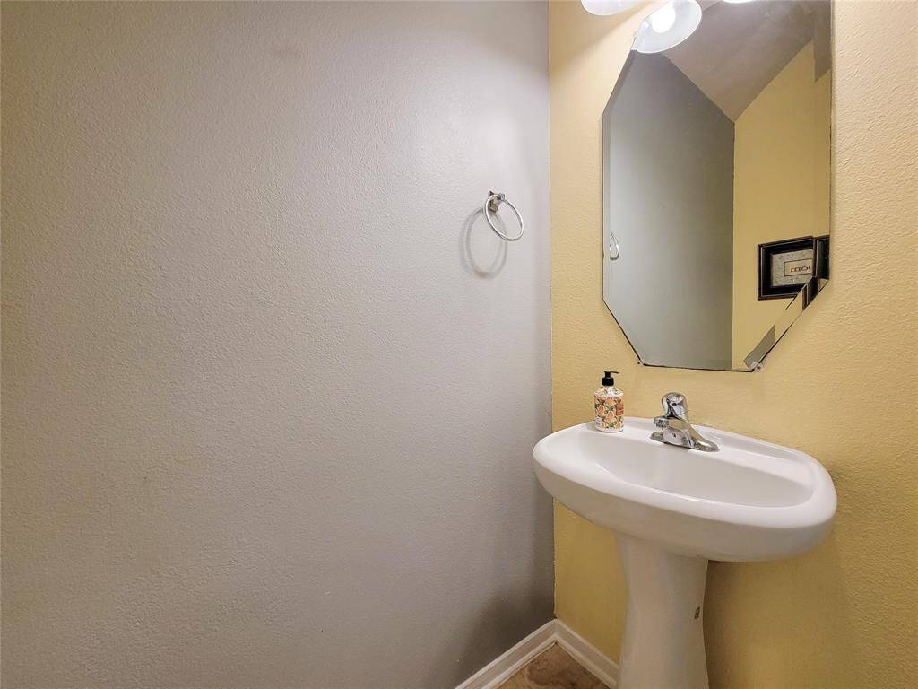 This bathroom features a large mirror with dual sinks, tile flooring, and a ceiling fan. It includes a tiled bathtub with natural light from a window, creating a bright and airy space.