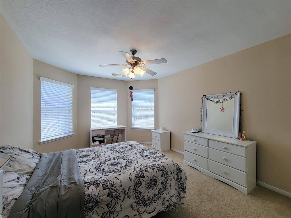 Overlooking the living room with high ceilings, a ceiling fan, and a fireplace. The room features large windows for natural light.