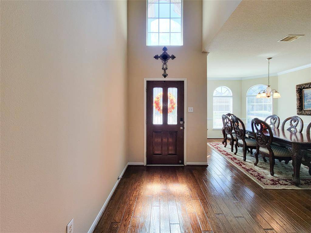 Bright entryway with a high ceiling and large window, leading into a formal dining room.
