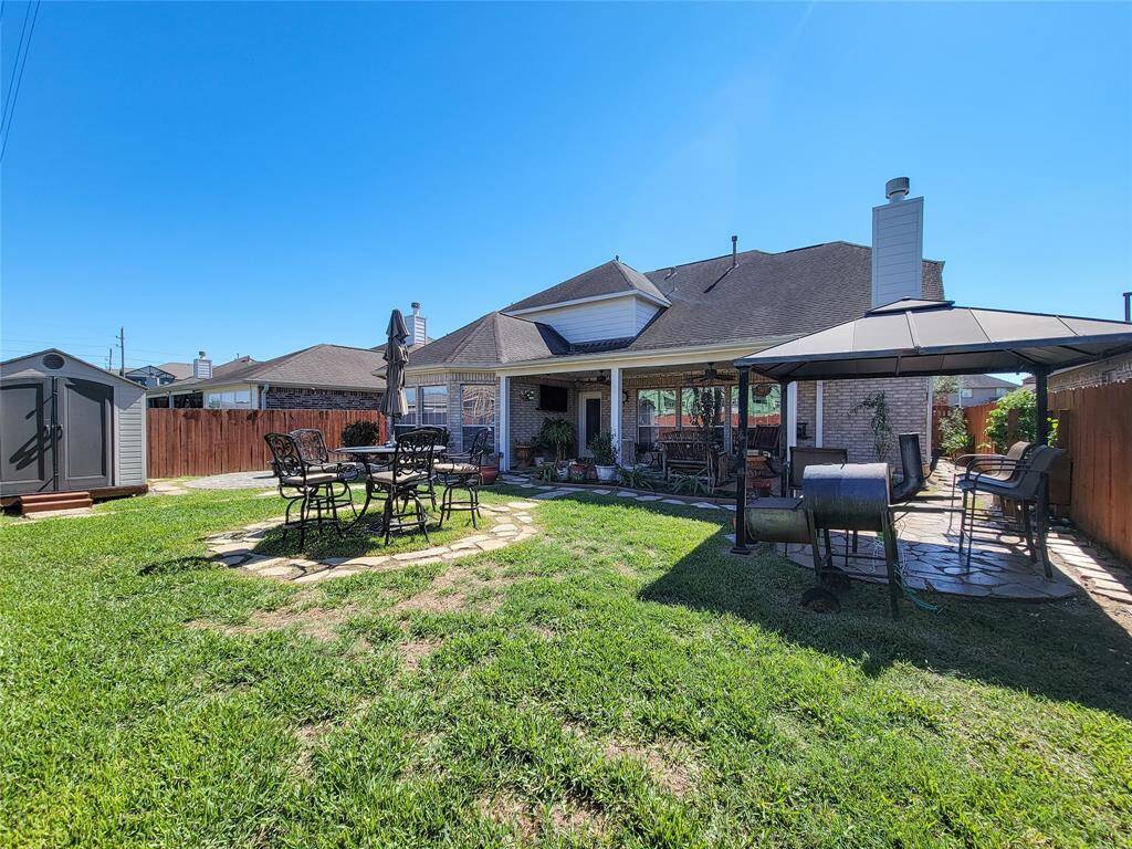 This backyard features a spacious lawn, a cozy covered patio area, perfect for entertaining A storage shed and privacy fence complete the space.