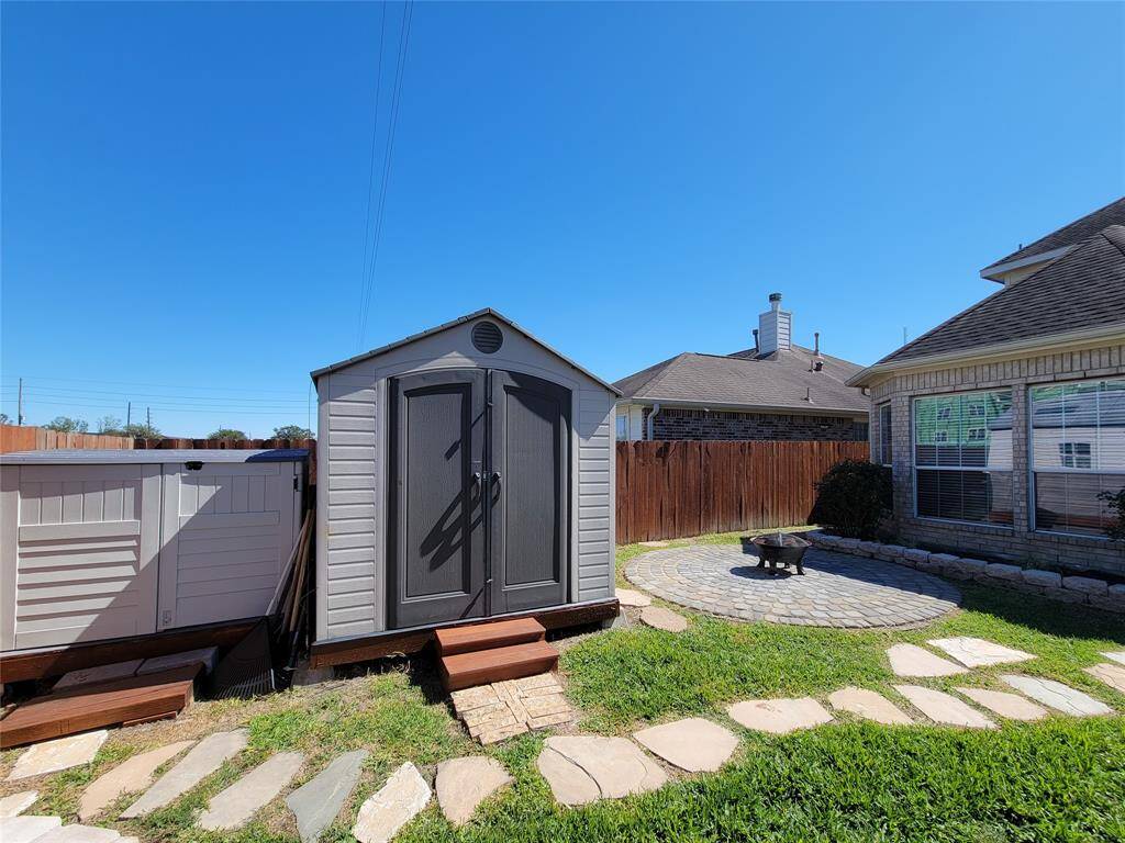 This backyard features stepping stones leading to a small storage shed. There's a round paved patio area, perfect for outdoor seating or a fire pit, and a wooden fence provides privacy.