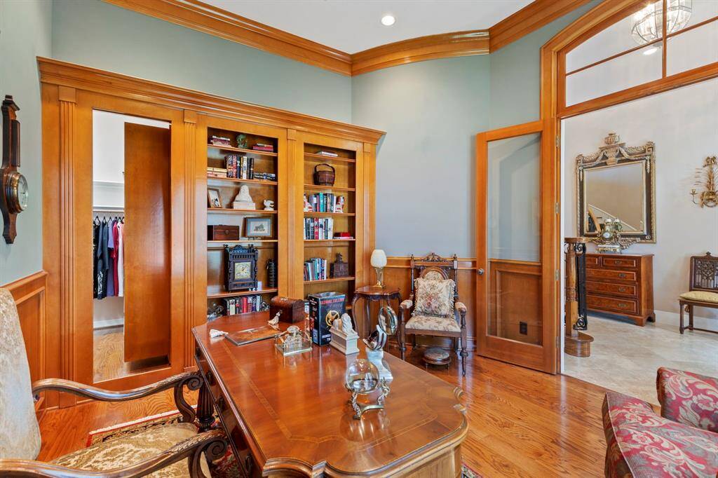 This photo showcases a well-appointed home office featuring elegant wooden built-in shelves filled with books and decor. The room includes sophisticated wooden floors and a bit of mystery with a hidden door in the book shelves.