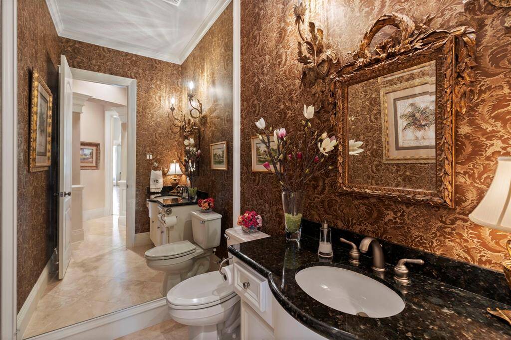 This elegant powder room features ornate wallpaper, a decorative mirror, and stylish lighting fixtures. The black granite countertop  adds a touch of luxury, while the neutral flooring complements the sophisticated design.