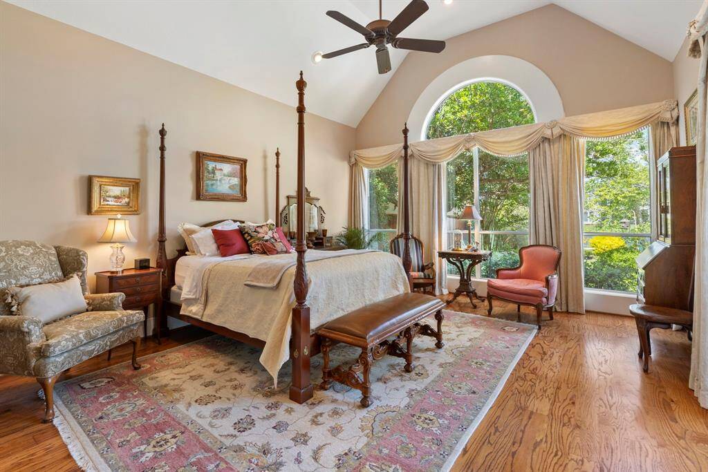 Spacious, elegant bedroom with vaulted ceiling and large arched window offering abundant natural light. Features hardwood floors, and a cozy seating area.