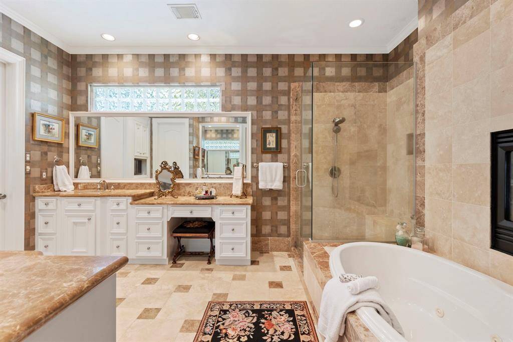 This elegant bathroom features a luxurious soaking tub, a spacious glass-enclosed shower, and a double vanity with ample storage. The stylish tile design and soft lighting create a warm, inviting atmosphere.