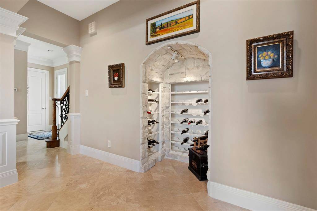 This photo showcases an elegant pass-through hallway with  tiled floor and a beautifully crafted wine cellar alcove featuring stone detailing.  This alcove is adjacent to the formal dining room and adds to the sophistication of this entertaining area.