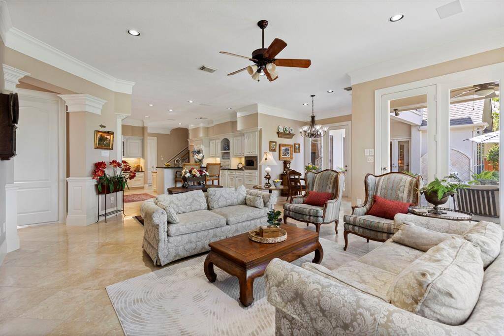 This spacious living area features a custom bookcase and entertainment center, a ceiling fan, and is encased by large windows allowing for natural light and relaxing views of the patio, gardens and the lake. The open layout flows seamlessly into the kitchen, creating a welcoming space perfect for entertaining and relaxation.
