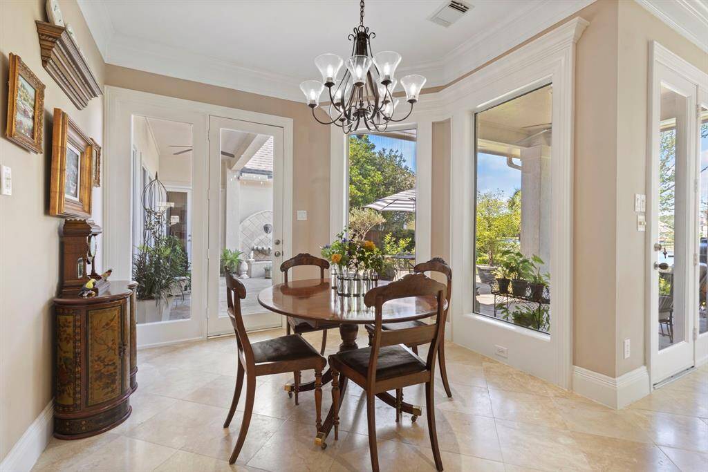 Bright dining area with large windows, elegant chandelier and French doors that open to a patio with greenery, enhancing the indoor-outdoor flow.