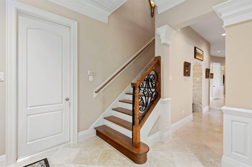 This photo showcases a stylish staircase with wrought iron balusters, and tasteful wall molding. This stairway leads to the upstairs quarters of the home.