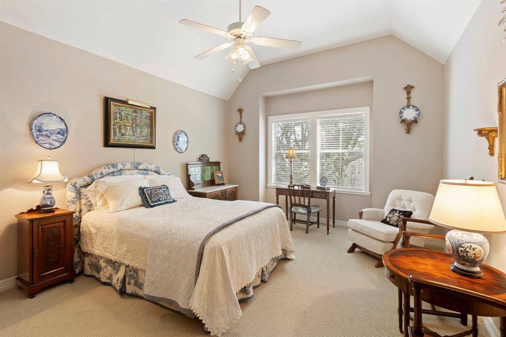 This expansive bedroom features a vaulted ceiling, neutral walls, and carpeted floors. It includes a large window providing natural light,  creating a warm and inviting atmosphere.