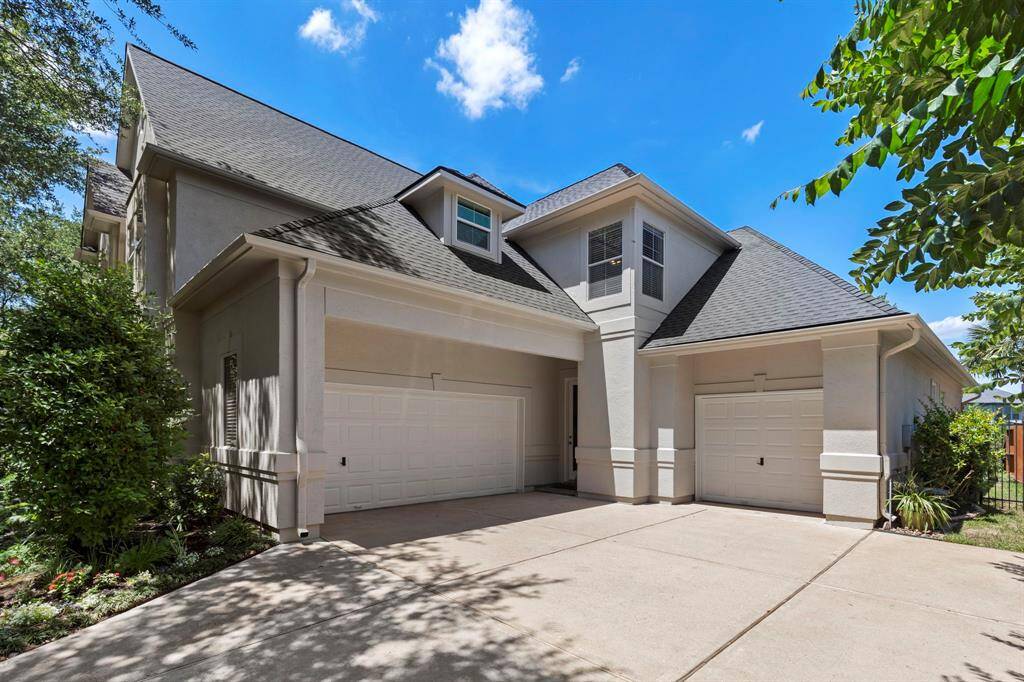 This home features a spacious driveway leading to a three-car garage, with a well-maintained exterior and lush landscaping. The roof is modern, and the property is surrounded by greenery, offering a welcoming and private atmosphere.