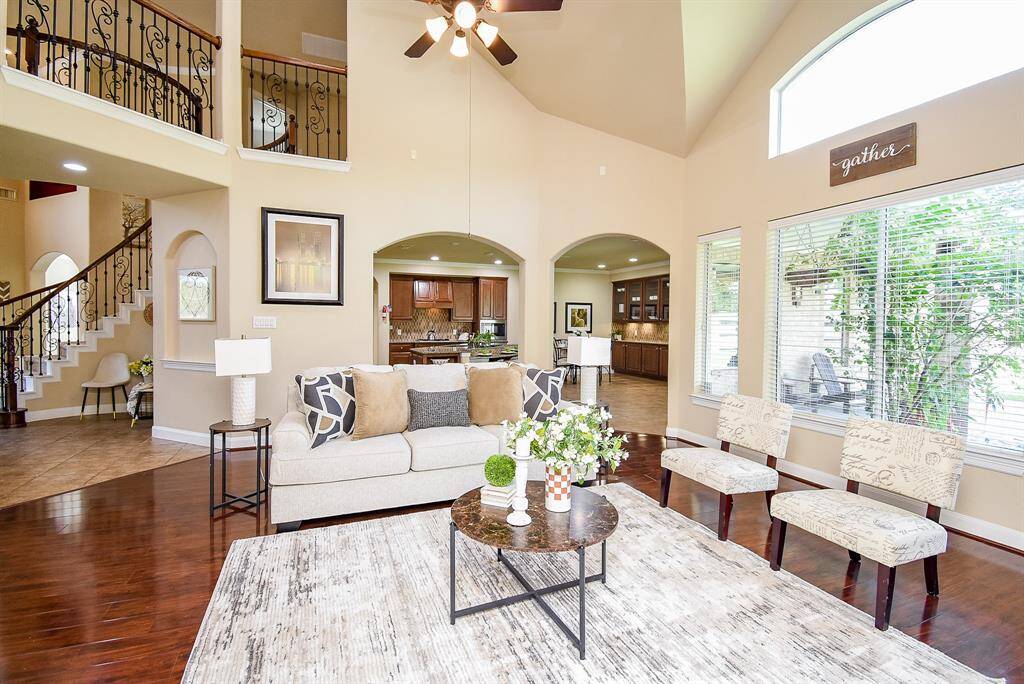 With soaring ceilings and two-story windows, this living area feels both expansive and warm. A fireplace adds a central focal point, while dual archways open to the kitchen, reinforcing the home’s natural flow.