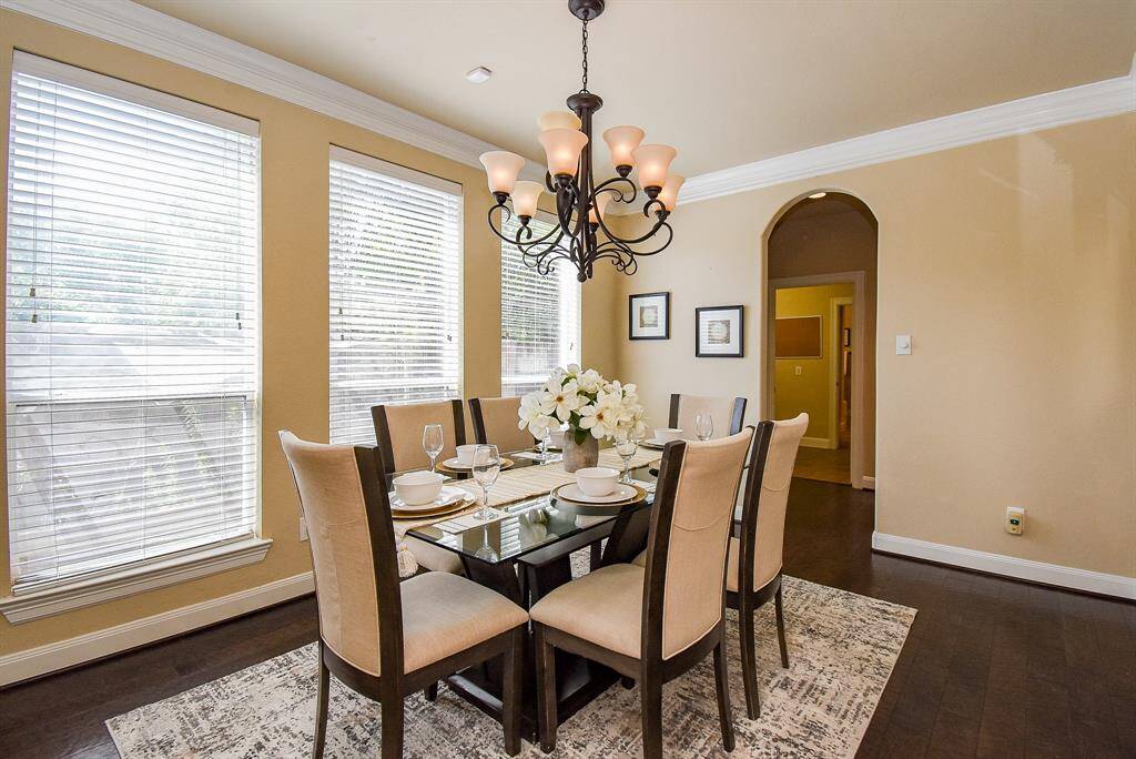 Oversized windows and dark hardwood floors create a striking backdrop in this refined dining space. A classic chandelier centers the room, offering ambiance for both weekday meals and special occasions.